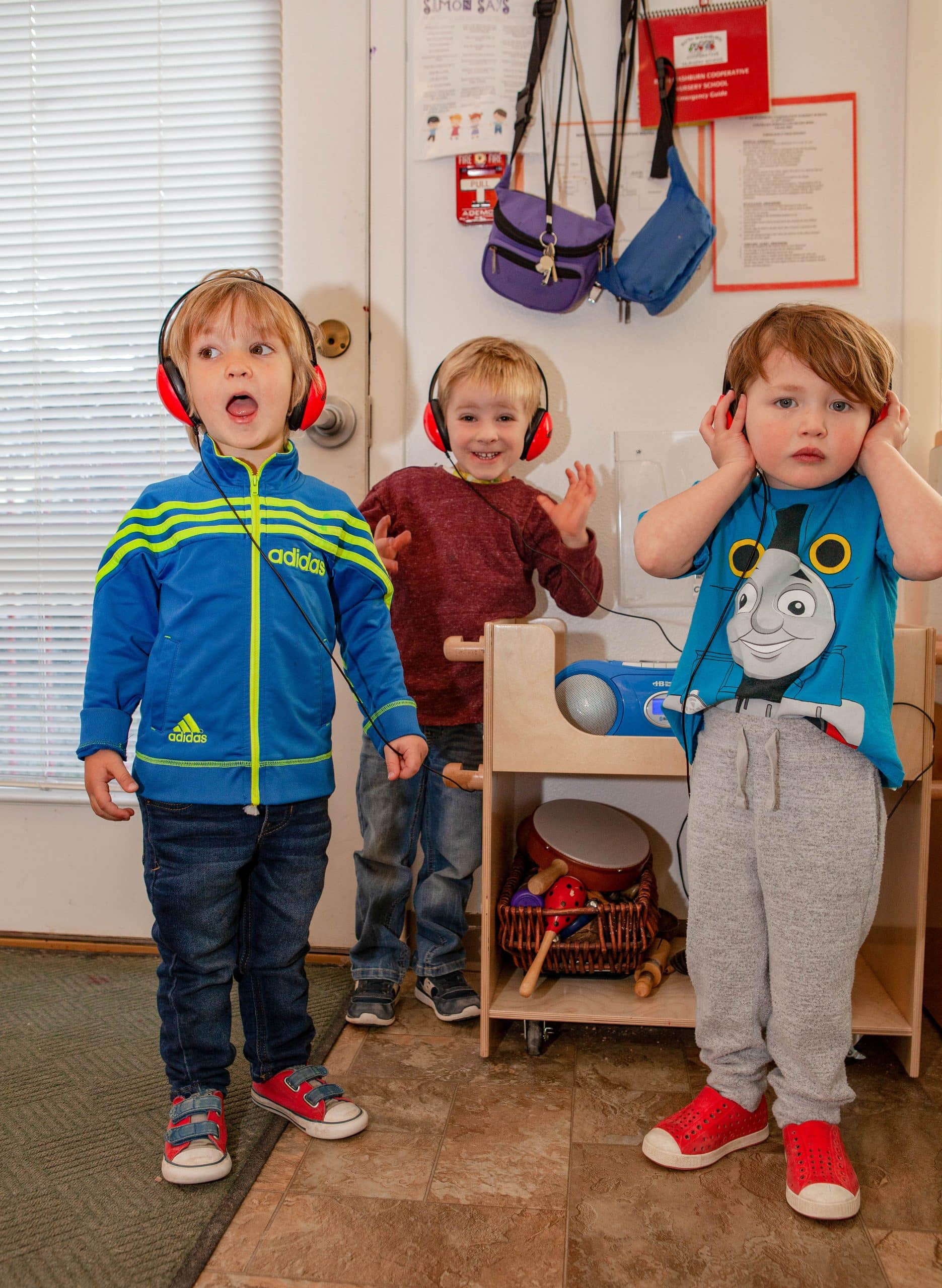 three children in colorful clothing wear red headphones while listenings to music