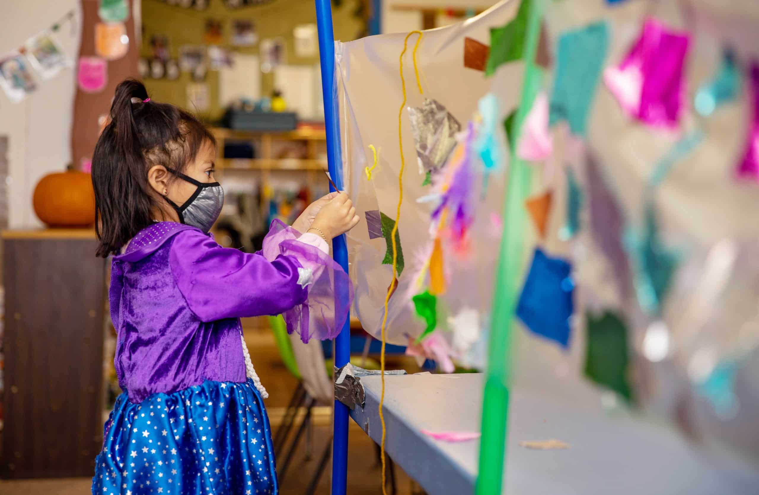 a girl in a bright purple dress sticks shapes to a clear piece of contact paper